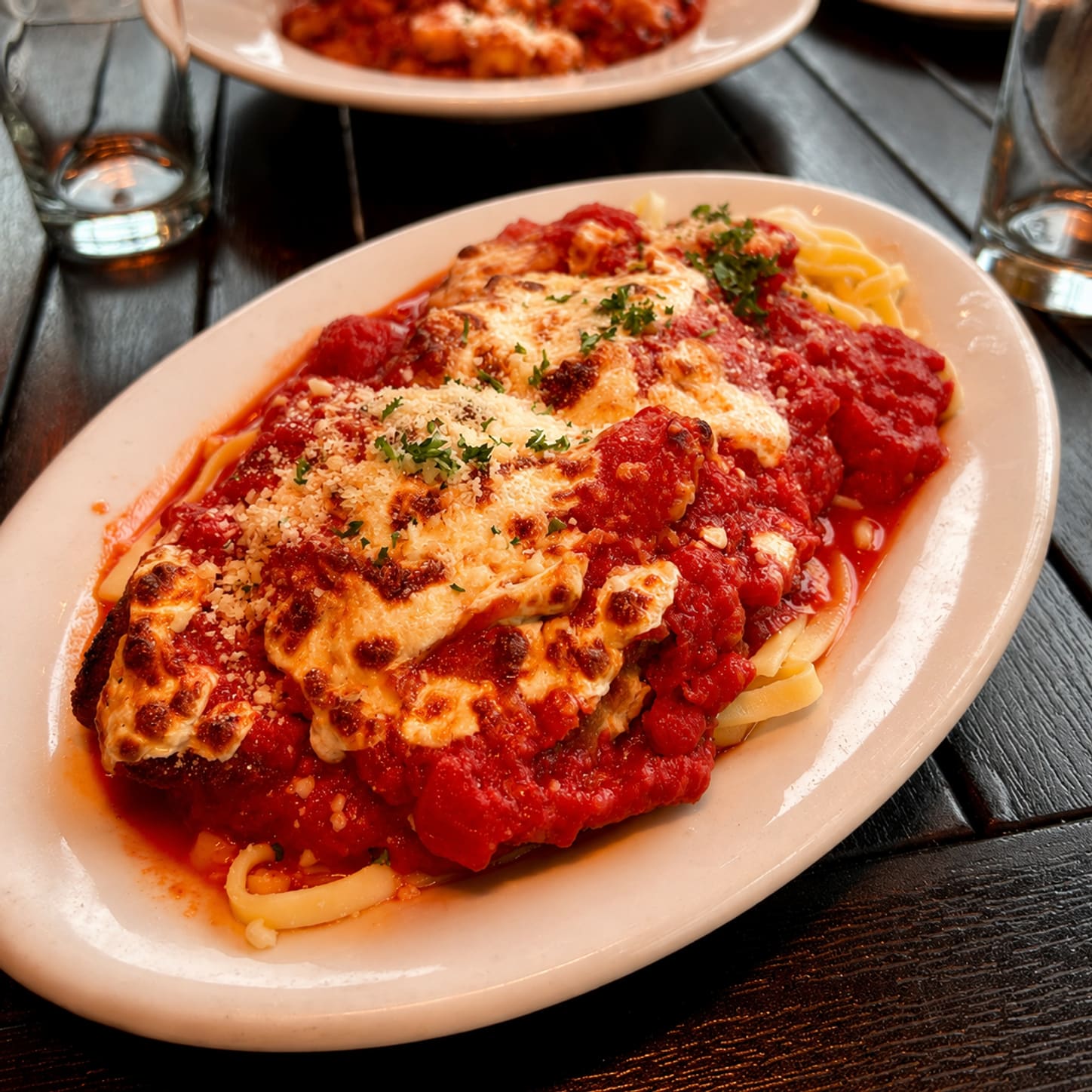 A breaded chicken cutlet on a bed of linguini, covered in marinara and melted fontina, on an oval white plate.